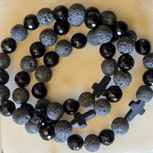 Op de afbeelding: Twee zwarte kralenarmbanden met zwarte kruisbedels. De armbanden zijn gemaakt van zwarte lavasteen en zwarte onyx kralen.