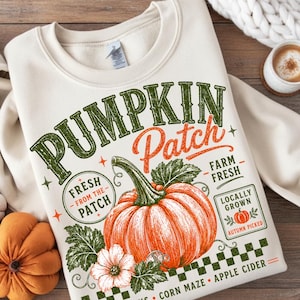 Könnte beinhalten: Ein cremefarbenes Sweatshirt mit Rundhalsausschnitt und einem Grafikdruck mit dem Text PUMPKIN Patch, FRESH FROM THE PATCH, FARM FRESH, LOCALLY GROWN, AUTUMN PICKED, CORN MAZE und APPLE CIDER sowie einem orangefarbenen Kürbis und grünen Blättern.