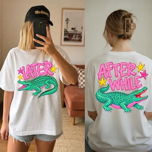 May include: A white t-shirt featuring a graphic of a green crocodile and the pink text "LATER" on the front, and the pink text "AFTER WHILE" with a green crocodile on the back. The design includes yellow and pink star accents on both sides.