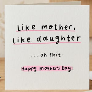 Może przedstawiać: Biała kartka z życzeniami z czarnym tekstem: „Jaka matka, taka córka... o kurde. Szczęśliwego Dnia Matki!” Tekst jest podkreślony na różowo. Kartka leży na drewnianej powierzchni z ołówkami i gumką.