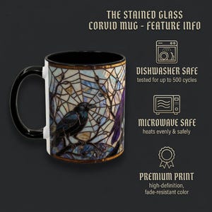 May include: A black and white ceramic mug with a stained glass design featuring a raven perched on a branch. The mug has a black handle and interior, with text that reads "THE STAINED GLASS CORVID MUG - FEATURE INFO".