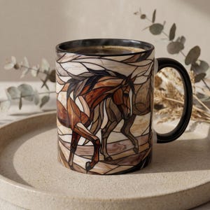 Puede incluir: Una taza de cerámica con una ilustración estilo vidriera de un caballo marrón en movimiento. La taza tiene un borde y un asa negros, con el diseño del caballo representado en tonos marrones, beige y crema con contornos oscuros.