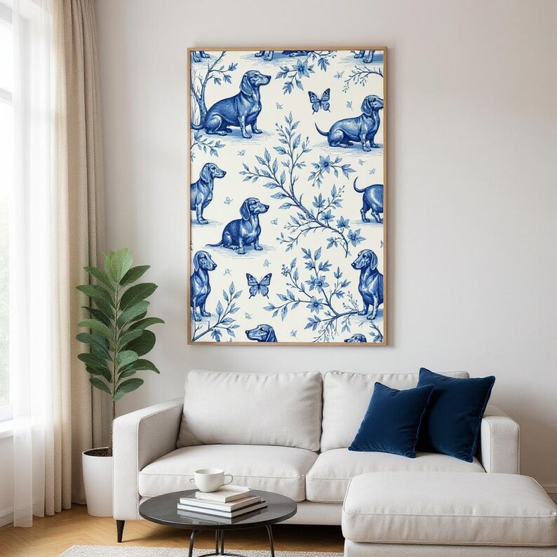 May include: A framed wall art print featuring a repeating pattern of blue dachshund dogs, butterflies, and floral elements on a cream background. The artwork is displayed in a living room setting with a white sofa, dark blue pillows, and a round coffee table.
