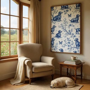 May include: A cozy living room scene featuring a beige armchair with a cream-colored throw, a small wooden side table, and a framed artwork. The artwork displays a blue and white pattern of dachshunds and butterflies. A sleeping puppy rests on a rug.