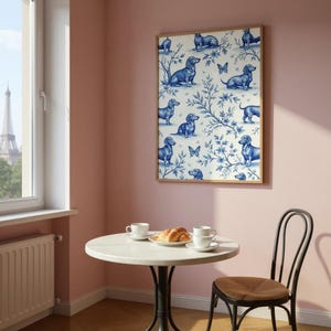 May include: A framed wall art print featuring a repeating pattern of blue dachshund dogs and butterflies on a white background with blue floral accents. The artwork is displayed on a pink wall above a small round table.
