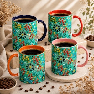 May include: Four ceramic mugs featuring a vibrant teal base with a raised, multi-colored floral pattern. Each mug has a distinct handle color: dark blue, red, orange, and light pink, with matching interior rims. The mugs are filled with dark coffee.