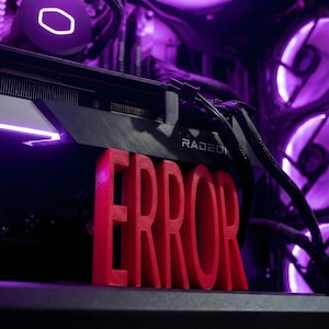 Puede incluir: Interior de una caja de ordenador iluminada con luces moradas. La palabra "ERROR" en rojo, impresa en 3D, destaca. Se ve una tarjeta gráfica Radeon, junto con ventiladores y otros componentes.