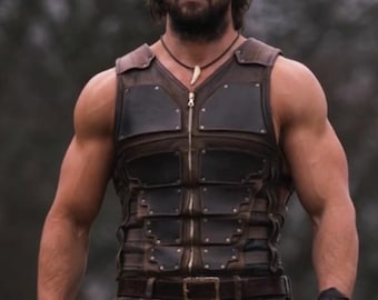 May include: A man wearing a brown leather vest with a zipper closure and a decorative bone pendant. The vest has a segmented design with multiple panels and is secured with a brown leather belt.
