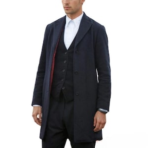 Op de afbeelding: Een marineblauwe overjas met een bijpassend vest en broek. De overjas heeft een klassiek ontwerp met een revers en een sluiting met drie knopen. Het vest heeft een sluiting met vijf knopen. Een wit overhemd maakt de outfit compleet.