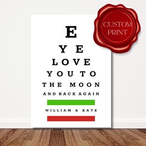 May include: A white print with black text in an eye chart style, reading "E YE LOVE YOU TO THE MOON AND BACK AGAIN." Green and red bars are at the bottom with the names "WILLIAM & KATE." A red wax seal with "CUSTOM PRINT" is in the upper right.
