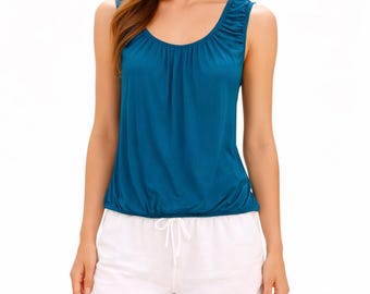 May include: A teal-colored tank top with a gathered neckline and a cinched waist is paired with white shorts. The shorts have a drawstring closure. The model is wearing casual summer clothing.