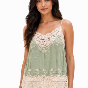 May include: Sage green camisole with delicate floral embroidery and cream-colored lace trim. The top features spaghetti straps and a scalloped lace hem. A stylish and feminine garment.