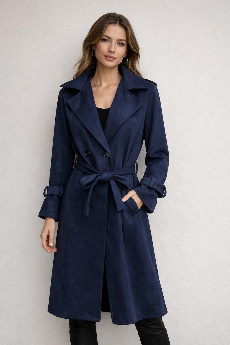 May include: A navy blue trench coat with a double-breasted design, a matching belt, and long sleeves. The coat features a classic collar, button details, and pockets. The model is wearing the coat.