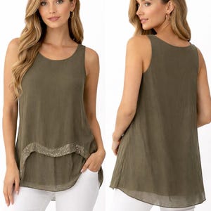 May include: Olive green sleeveless top with a scoop neckline and a sequined band detail. The top has a flowing, layered design and is paired with white trousers. The model is wearing gold hoop earrings.