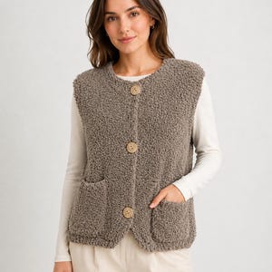 Puede incluir: Un chaleco sin mangas de color topo hecho de un material de forro polar rizado y texturizado. El chaleco presenta un cuello redondo, tres botones circulares grandes en la parte delantera central y dos bolsillos de parche en la cintura.