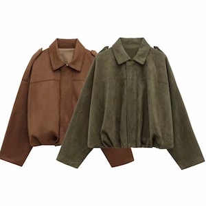 May include: Two suede jackets, one in a rich brown and the other in olive green, are displayed. Both jackets have a classic collar, shoulder epaulettes, and a relaxed fit. The jackets are a stylish outerwear option.