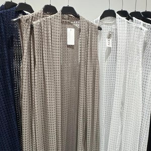 Könnte beinhalten: Eine Reihe ärmelloser Oberteile in verschiedenen Farben, darunter Marineblau, Taupe, Weiß und Schwarz, hängen an schwarzen Kleiderbügeln. Jedes Oberteil hat ein sich wiederholendes kreisförmiges Muster. Die Oberteile werden vor einem neutralen Hintergrund präsentiert.