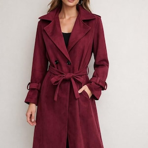 May include: A burgundy trench coat with a double-breasted front, a matching belt, and long sleeves. The coat features a notched collar, pockets, and buttoned cuffs. The coat is approximately 140 cm long.