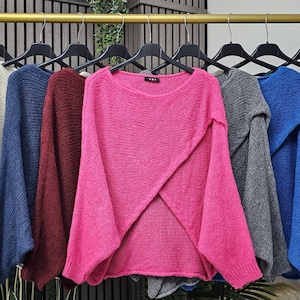 Puede incluir: Una colección de suéteres en varios colores, incluyendo azul marino, crema, azul, burdeos y rosa, colgados en una percha. Los suéteres tienen mangas largas y un corte holgado, con una variedad de escotes.