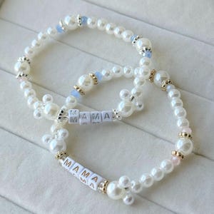 Può includere: Due braccialetti di perline composti da finte perle bianche, piccole perline decorative azzurre e rosa e distanziatori dorati. Ogni braccialetto include perline quadrate bianche con lettere che compongono la parola MAMA e grappoli di perle a forma di Mickey Mouse.