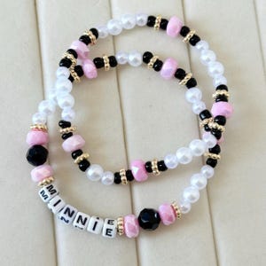 Puede incluir: Dos pulseras de cuentas con detalles blancos, rosas, negros y dorados. Una pulsera deletrea "MINNIE" con cuentas de letras blancas. Las pulseras presentan cuentas tipo perla y formas geom&eacute;tricas.