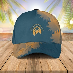 May include: A blue baseball cap with a curved brim and a black button on top. The cap features a logo with a palm tree and the text "FloridianHome.ca" in orange. The design includes orange starburst patterns.