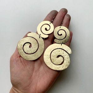 May include: A pair of gold-toned earrings with a spiral design. The earrings are made of hammered metal and have a textured finish.