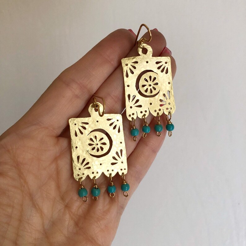 May include: Gold earrings with a cutout design and turquoise beads. The earrings are shaped like a square with a crescent moon and flower design.