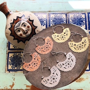 May include: Five pairs of handmade earrings with a cut-out floral design. The earrings are made of metal and come in copper, gold, and silver tones.