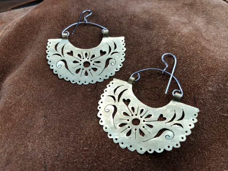 May include: A pair of silver hoop earrings with a delicate, intricate floral design. The earrings are made of metal and have a cutout pattern.