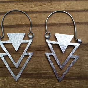 May include: A pair of silver earrings with a hammered triangle design. The earrings are made of metal and have a simple, geometric shape.