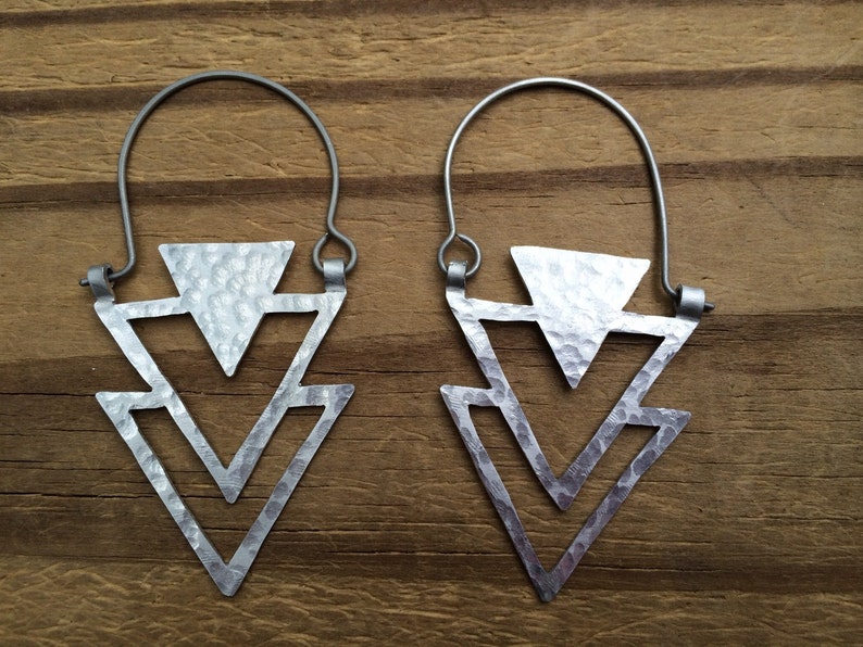 May include: A pair of silver earrings with a hammered triangle design. The earrings are made of metal and have a simple, geometric shape.