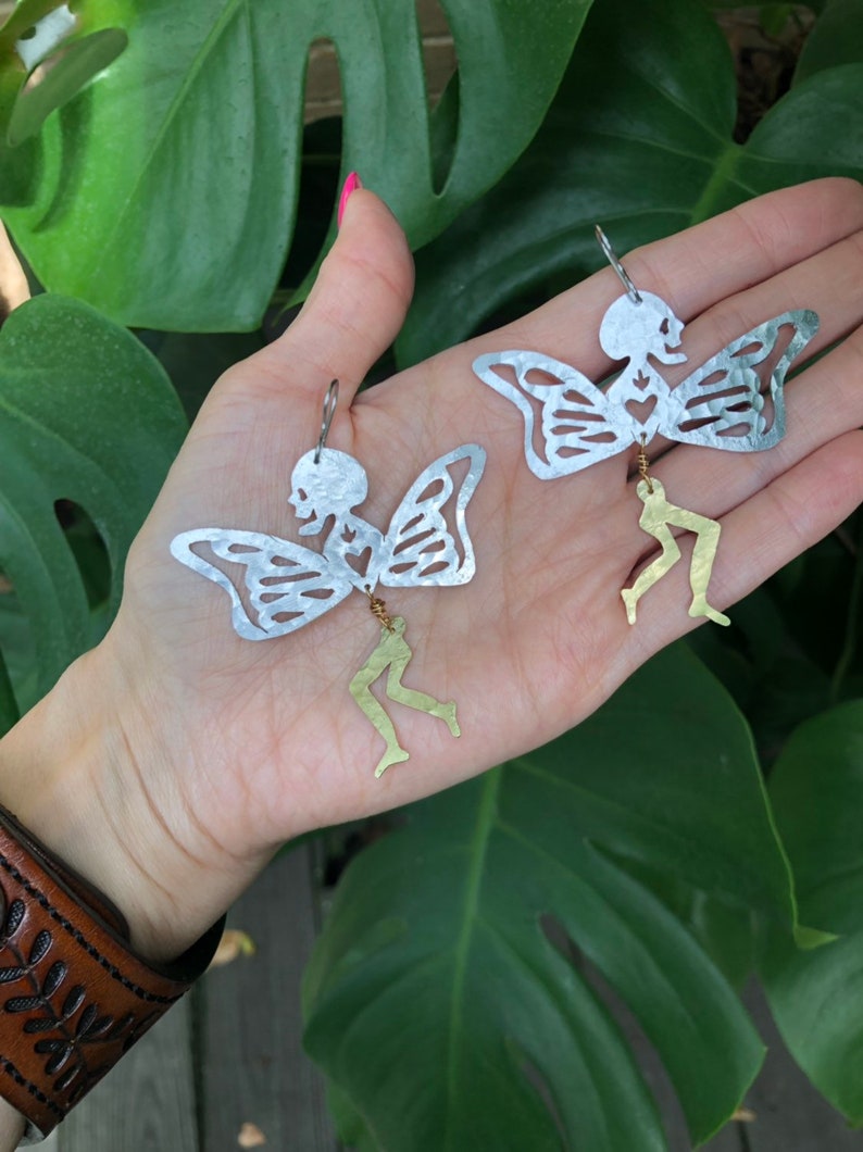 Pode incluir: Um par de brincos de borboleta esqueleto prateados com pernas douradas penduradas. Os brincos s&atilde;o feitos &agrave; m&atilde;o e t&ecirc;m um design delicado e caprichoso.