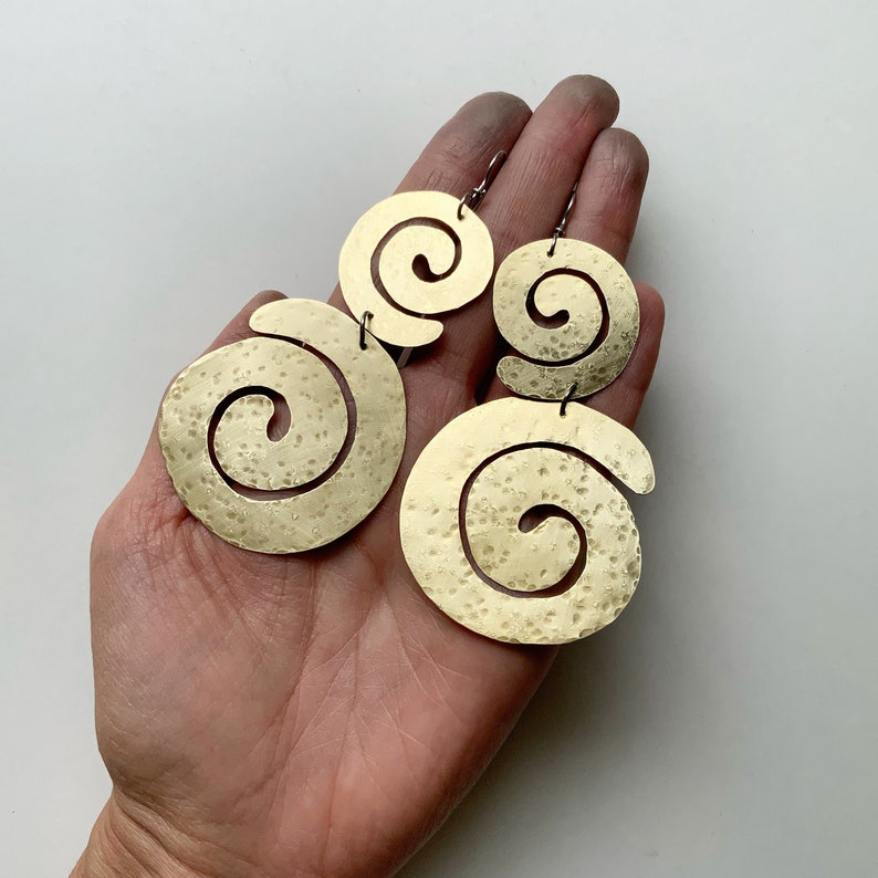 May include: A pair of gold-toned earrings with a spiral design. The earrings are made of hammered metal and have a textured finish.