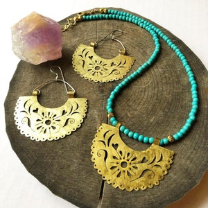 May include: A turquoise beaded necklace with a brass pendant and matching earrings. The pendant and earrings are cut-out designs with floral and heart motifs.