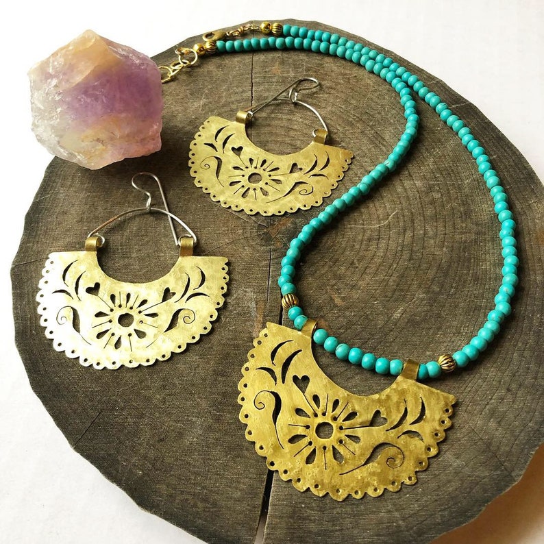 May include: A turquoise beaded necklace with a brass pendant and matching earrings. The pendant and earrings are cut-out designs with floral and heart motifs.