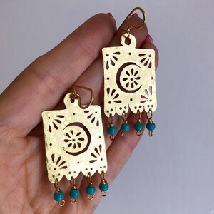 May include: Gold earrings with a cutout design and turquoise beads. The earrings are shaped like a square with a crescent moon and flower design.