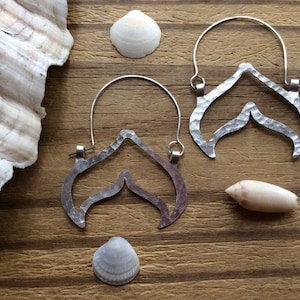 May include: A pair of silver earrings with a unique wave-like design. The earrings are made of hammered metal and have a rustic, handmade look.