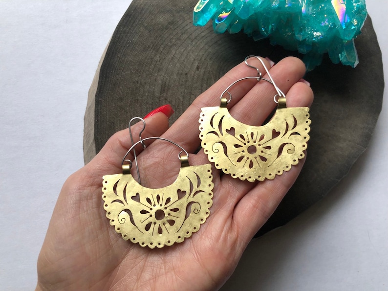 May include: A pair of gold-toned brass earrings with a delicate floral design. The earrings are shaped like half-circles and have a scalloped edge.