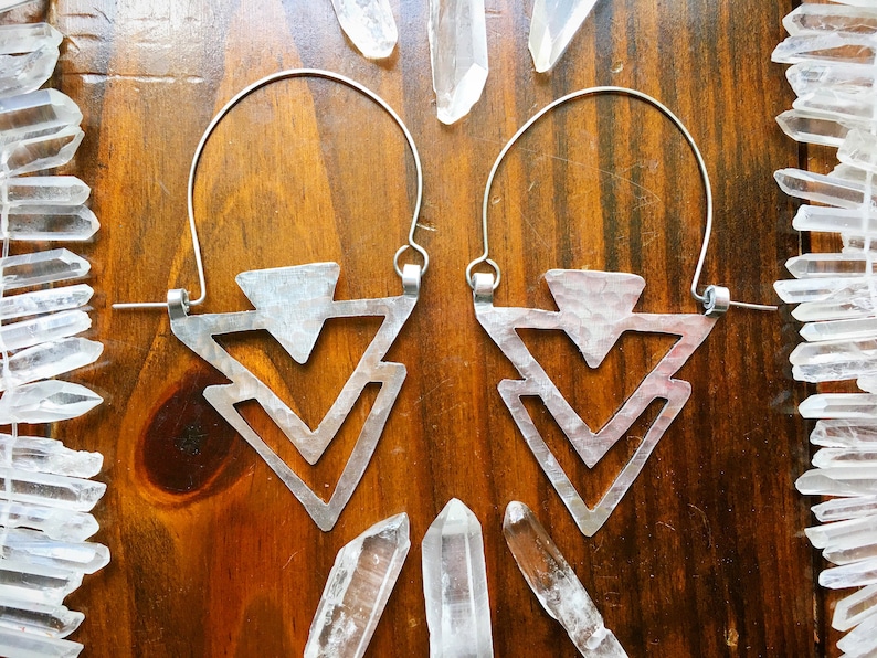 May include: A pair of silver geometric earrings with a triangular design. The earrings are made of metal and have a hammered finish.