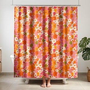 Peut inclure: Un rideau de douche arborant un motif dense et répétitif de fleurs dans des tons orange, rose, blanc et vert olive. Le tissu est suspendu à une tringle métallique par des anneaux, présentant un design floral multicolore sur toute la surface.