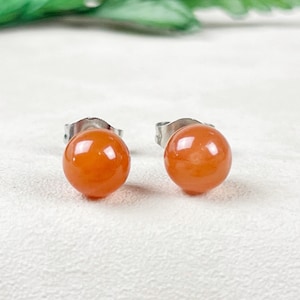 May include: A pair of orange gemstone stud earrings with silver posts.