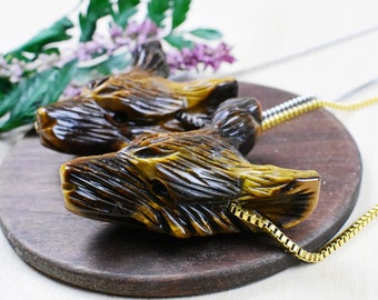 May include: Two carved tiger's eye wolf head pendants on a gold chain. The pendants are brown and gold with intricate details.