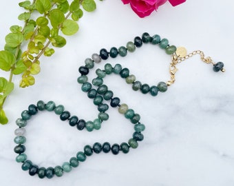 May include: A green agate beaded necklace with a gold clasp. The necklace is on a white marble surface.
