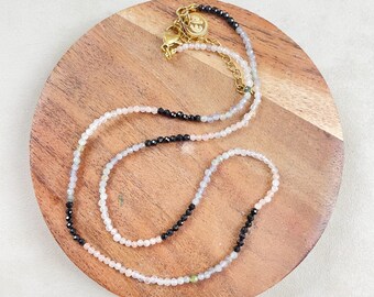 Peut inclure: Un collier délicat avec des perles noires, blanches et rose pâle. Le collier est composé de petites perles rondes et possède un fermoir doré.