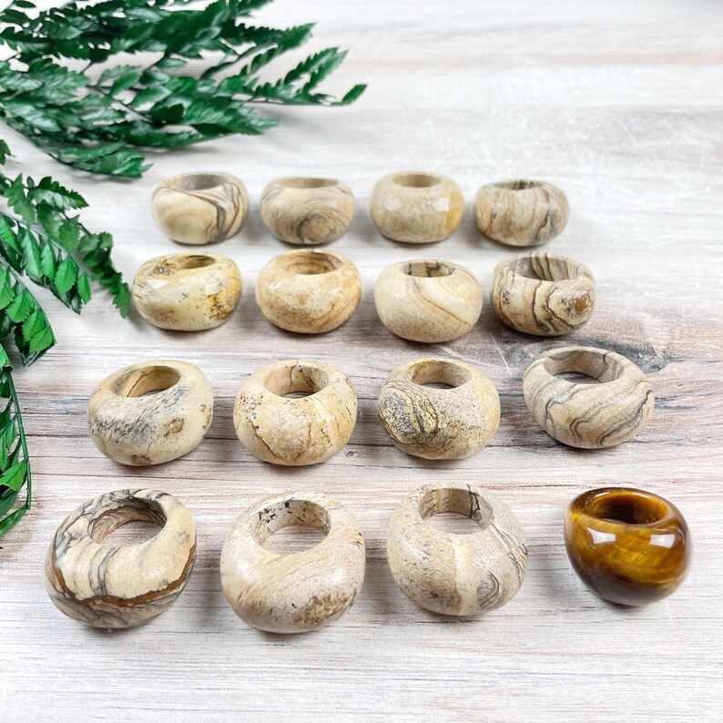 May include: A collection of 15 smooth, round, beige and brown banded stone rings, with one additional ring in a tiger's eye pattern.