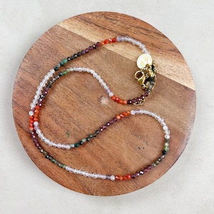 May include: A multi-colored beaded necklace with a gold clasp. The necklace features beads in shades of pink, orange, green, and brown.
