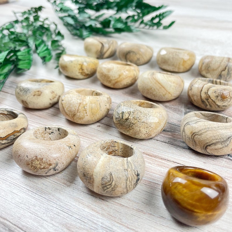 May include: A collection of 13 smooth, beige and brown banded rings made of fossilized wood. One ring is a golden brown tiger's eye.