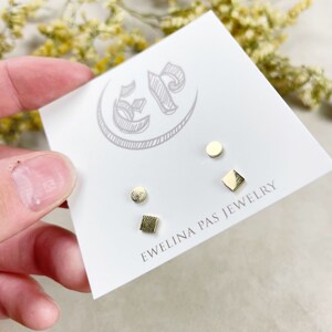 May include: A set of three gold stud earrings in different geometric shapes: a circle, a square, and a rectangle. The earrings are displayed on a white card with the text "Ewelina Pas Jewelry".