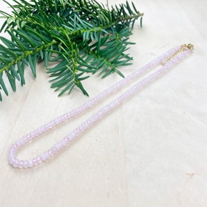 May include: A delicate pink beaded necklace with a gold clasp. The necklace is made of small, round beads and is approximately 18 inches long.